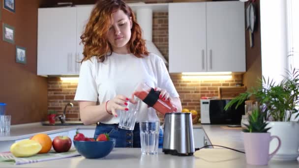 Een jonge vrouw thuis in de keuken maakt fruit smoothie. Mooie gelukkige jonge vrouw in casual home keuken bereidt fitness cocktail thuis. Sportief en veganistisch meel - Video