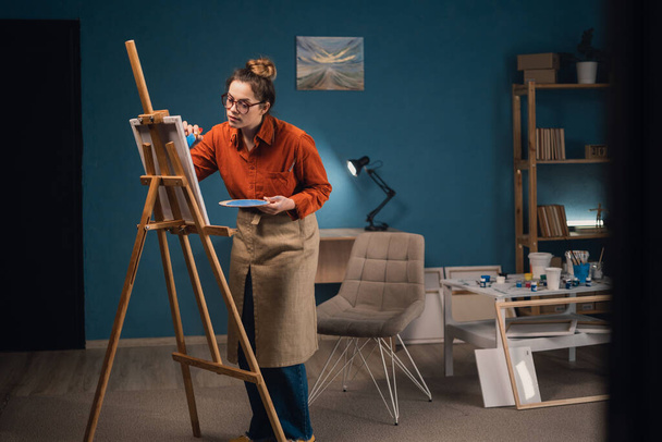 Naistaiteilija maalaamassa taidekuvaansa kankaalle kotona. Harrastus- ja vapaa-ajan konsepti. Kopioi tila - Valokuva, kuva
