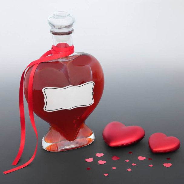 Love potion magical concoction or perfume gift in heart shaped bottle with red heart decorations on gradient gray. Valentines Day lovers abstract concept. - Photo, Image