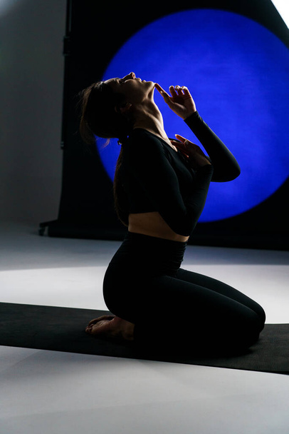 スタジオでヨガをしたり,バックグラウンドで軽いイルミネーションを背景にポーズをする運動女性. ヨガと瞑想のコンセプト - 写真・画像