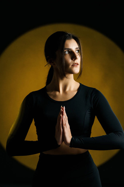 Femme sportive faisant du yoga en studio et posant sur fond d'illuminations lumineuses en arrière-plan. Yoga et concept de méditation - Photo, image
