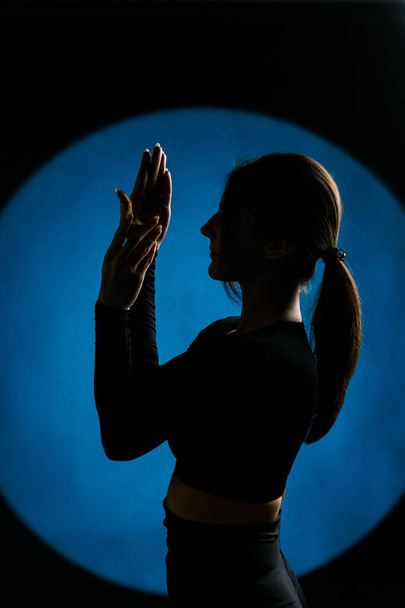 Sportowa kobieta uprawiająca jogę w studio i pozująca na tle świetlnych iluminacji w tle. Koncepcja jogi i medytacji - Zdjęcie, obraz