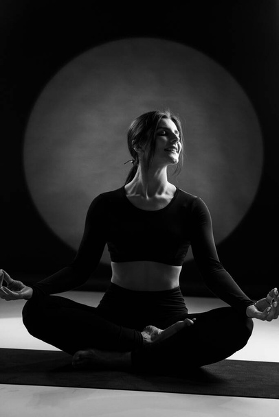 Athletic woman doing yoga in the studio and posing against the backdrop of light illuminations in the background. Yoga and meditation concept - Photo, Image