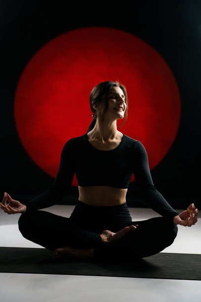 Mujer atlética haciendo yoga en el estudio y posando sobre el telón de fondo de iluminaciones de luz en el fondo. Concepto de yoga y meditación - Foto, Imagen