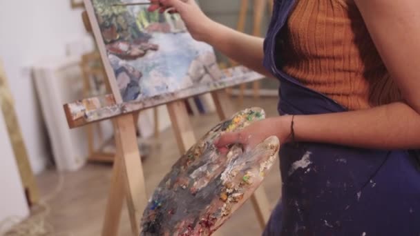 Μια γυναίκα κρατάει ένα πινέλο και ζωγραφίζει σε ένα καβαλέτο. - Πλάνα, βίντεο