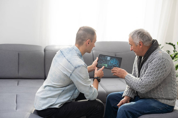 Kuva eurooppalaisesta lääkäristä puhumassa iäkkään miespotilaan kanssa ja istumassa studiossa, eristyksissä valkoisella pohjalla. Laadukas kuva - Valokuva, kuva