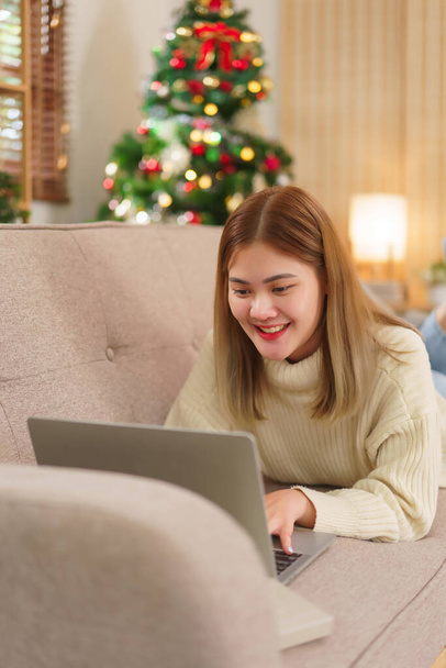 Концепция зимних праздников, женщины, лежащие на диване и серфинг социальные сети на ноутбуке со счастьем. - Фото, изображение