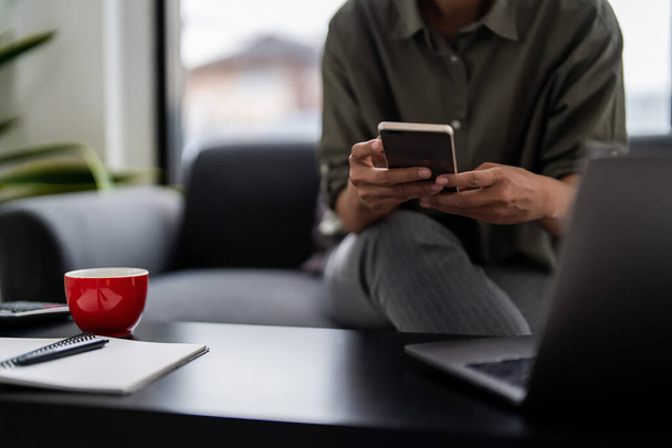 アジアのカジュアルなビジネスマンは,成長ファイナンスを読んでソファに座ってスマートフォンで新しいスタートアップレポート. - 写真・画像
