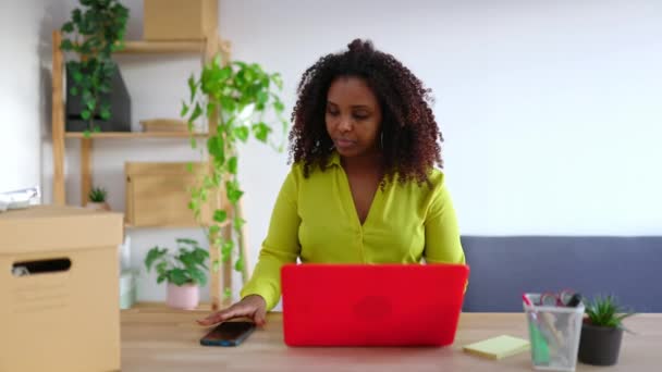 Wesoła afrykańska biznesmenka pracująca na laptopie w magazynie przygotowująca pudełko z przesyłkami w małym biurze biznesowym. Koncepcja przedsiębiorców. - Materiał filmowy, wideo