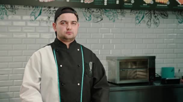 Retrato de un fabricante de sushi masculino serio en una gorra en el fondo de la cocina profesional - Metraje, vídeo