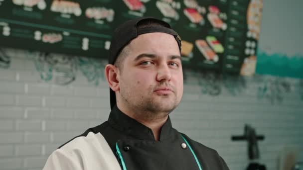 Portrét seriózního muže sushi výrobce v čepici na pozadí profesionální kuchyně - Záběry, video