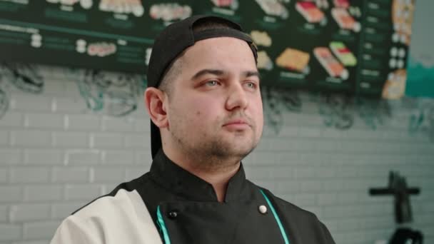 Portrét seriózního muže sushi výrobce v čepici na pozadí profesionální kuchyně - Záběry, video