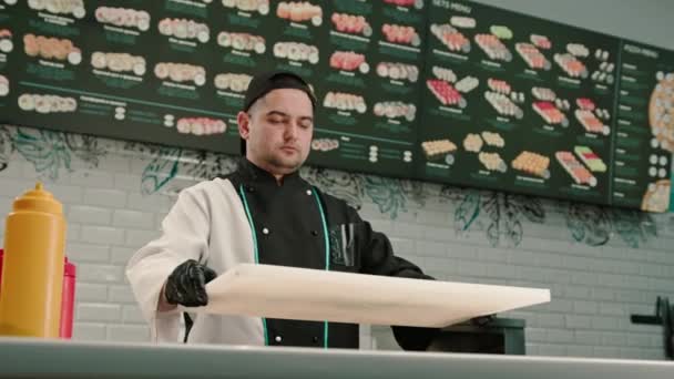 Retrato de um fabricante de sushi masculino grave em um boné no fundo da cozinha profissional - Filmagem, Vídeo