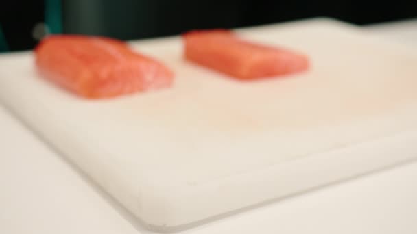Primo piano di un filetto di salmone adagiato su un tavolo da cucina bianco nella cucina del ristorante di sushi - Filmati, video