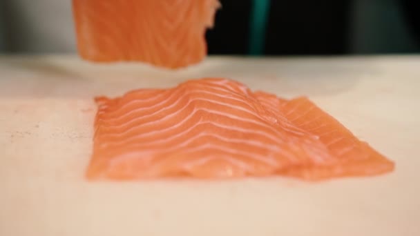 Primo piano dello chef di sushi che mette pezzi di filetto di salmone sul tagliere mentre cucina il ristorante di sushi - Filmati, video