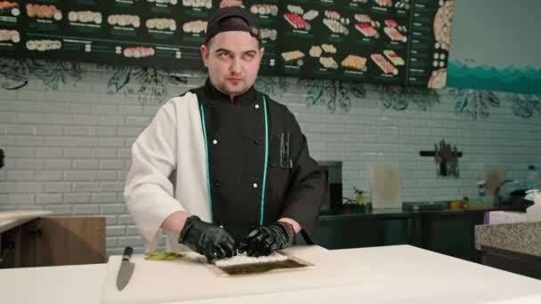 a sushi szef kuchni w czarnych rękawiczkach przygotowanie sushi przy użyciu ryżu Nori arkuszy krewetki filet krewetki ser twarożek ogórek awokado na stole kuchnia - Materiał filmowy, wideo