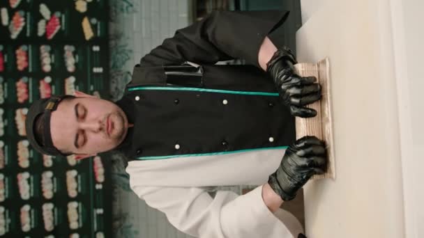 vertikální video Sushi šéfkuchař připravuje lahodný krevetový závitek s lososem a chuka mořské řasy na bambusové sushi podložce - Záběry, video