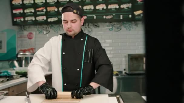 El chef de sushi prepara queso crema con salmón y pepino en una pizarra de cocina blanca - Metraje, vídeo