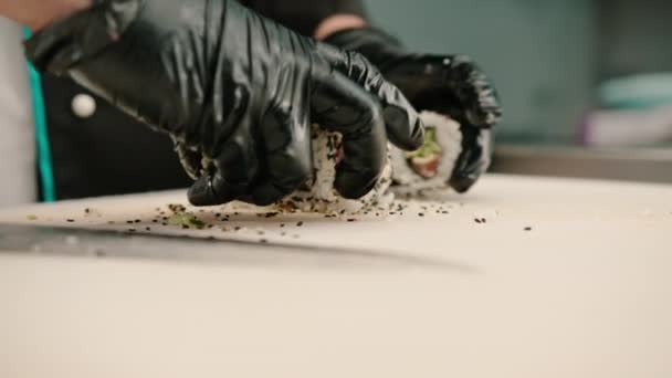 Sushi-Koch schneidet in der Restaurantküche eine köstliche Semmel in Sesam mit Lachs und Gurke mit einem Messer in Großaufnahme - Filmmaterial, Video