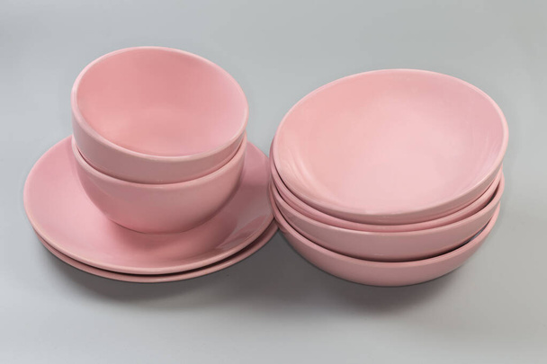 Zestaw szklanych ceramicznych różowych głębokich i szerokich płytkich misek do serwowania żywności i płaskich płyt serwisowych w stosach na szarym tle - Zdjęcie, obraz