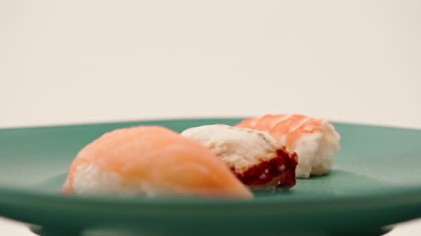 Крупный план трех нигирийских суши с лососем-угрем и креветками, лежащих на синей красивой тарелке на белом фоне - Кадры, видео