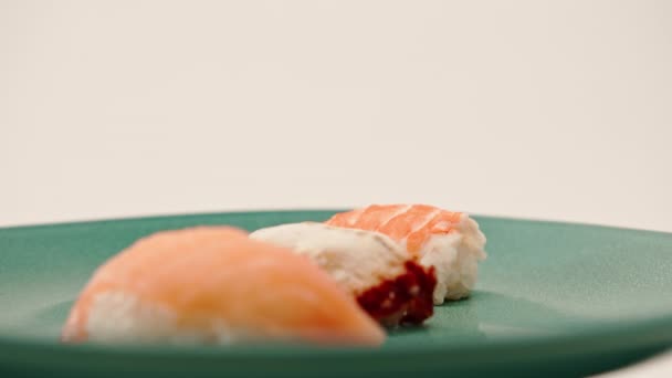 白い背景に青い美しいプレートの上にウナギサーモンとエビが横たわった3匹のニギリ寿司のクローズアップ - 映像、動画