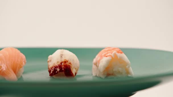 白い背景に青い美しいプレートの上にウナギサーモンとエビが横たわった3匹のニギリ寿司のクローズアップ - 映像、動画