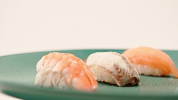 Крупный план трех нигирийских суши с лососем-угрем и креветками, лежащих на синей красивой тарелке на белом фоне - Кадры, видео
