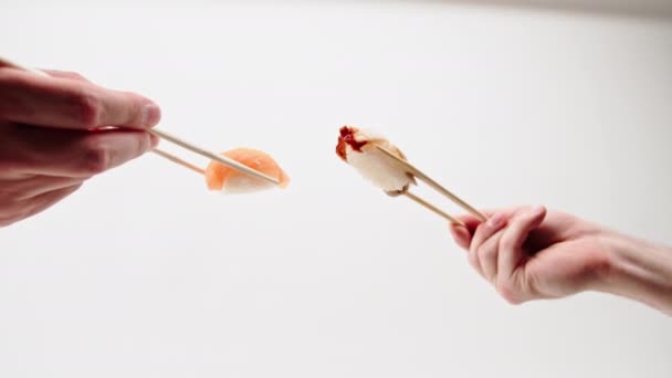 Gros plan des mains des hommes avec des baguettes tenant sushis d'anguille et sushis de saumon dans l'air devant l'autre sur un fond blanc - Séquence, vidéo