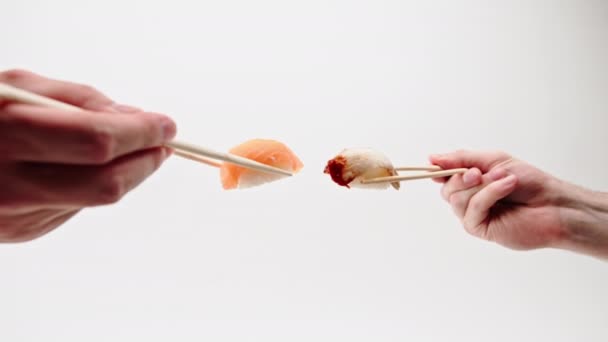 Großaufnahme von Männerhänden mit Essstäbchen, die Aal-Sushi und Lachs-Sushi vor weißem Hintergrund in der Luft halten - Filmmaterial, Video