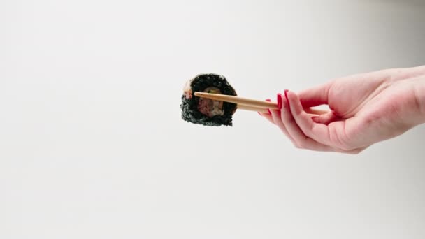 Close-up de sushi com arroz preto e enguia que o homem segura com pauzinhos em um fundo branco - Filmagem, Vídeo