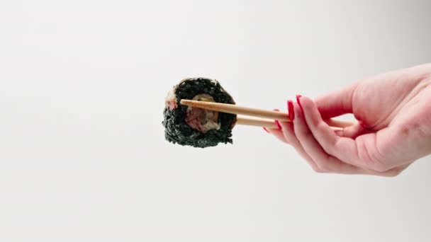 Zbliżenie sushi z czarnym ryżem i węgorzem, które człowiek trzyma pałeczkami na białym tle - Materiał filmowy, wideo