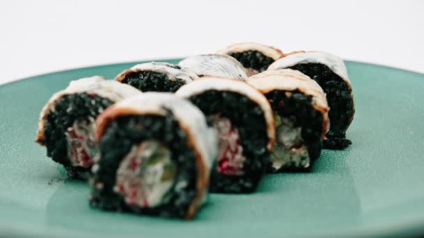 Eine Nahaufnahme schwarzer Reisaalrollen auf einem schönen blauen Teller Das Konzept, das Sushi und asiatisches Essen liebt - Filmmaterial, Video