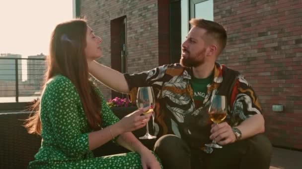 Νεαρό ζευγάρι άντρας και γυναίκα με ποτήρια κρασί στα χέρια να κουβεντιάζουν και να τρώνε ρολά σούσι καθισμένοι στη βεράντα με θέα την πόλη - Πλάνα, βίντεο