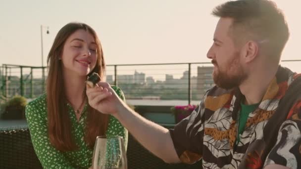 Fiatal pár férfi tartja sushi evőpálcikával, és táplál egy gyönyörű lány a teraszon közben egy dátum aranyos beszélgetés nevetés - Felvétel, videó