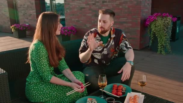 Mladý pár muž drží sushi s hůlkami a krmí krásnou dívku na terase během rande roztomilý chatování smích - Záběry, video