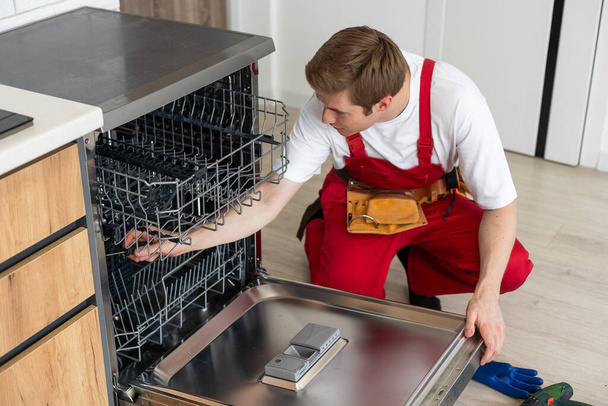 A szerelő ellenőrzi a mosogatógép működési állapotát a konyhában. - Fotó, kép