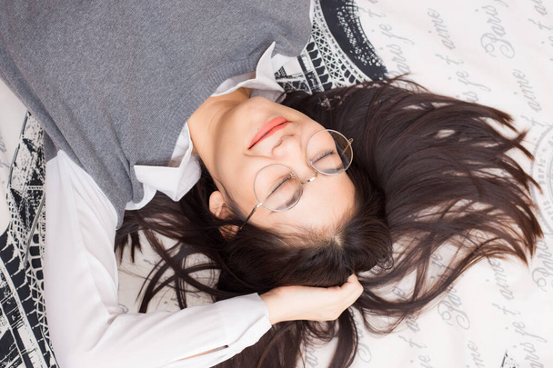 Очки женщины расслабляются лежа на кровати белое одеяло
 - Фото, изображение