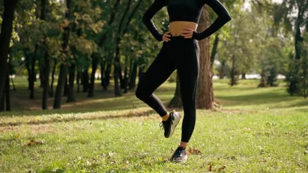 Sportowa dziewczyna podczas porannego treningu na świeżym powietrzu wykonuje koliste ruchy nogą rozciągając staw biodrowy - Materiał filmowy, wideo