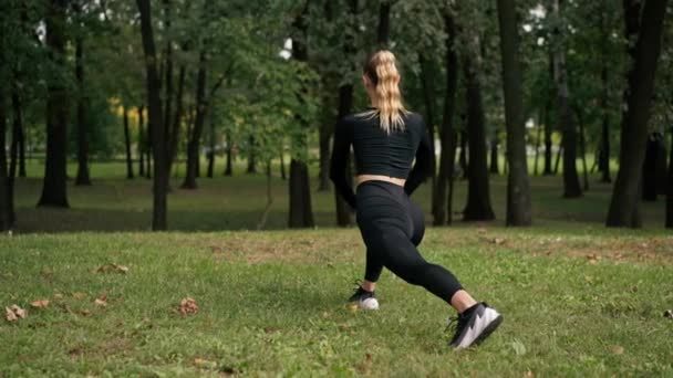 Jovem em sportswear fazendo exercício lunge para treinar equilíbrio e esticar os músculos da perna da coxa visão traseira - Filmagem, Vídeo