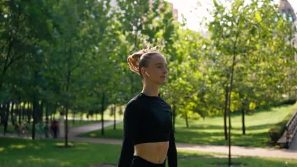 Tyttö urheilija suorittaa hyppyharjoituksia kuin lämmittely ennen koulutusta kadulla vihreä kesäpuisto - Materiaali, video