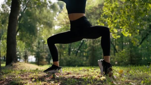 Close-up of Athlete girl wykonuje ćwiczenia dla nóg przysiady treningowe podczas porannych ćwiczeń w parku aktywnego stylu życia - Materiał filmowy, wideo
