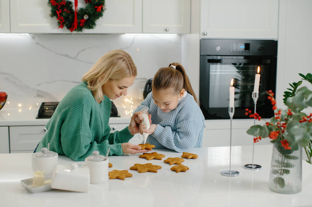 Madre e figlia decorano i biscotti di Natale in cucina. - Foto, immagini