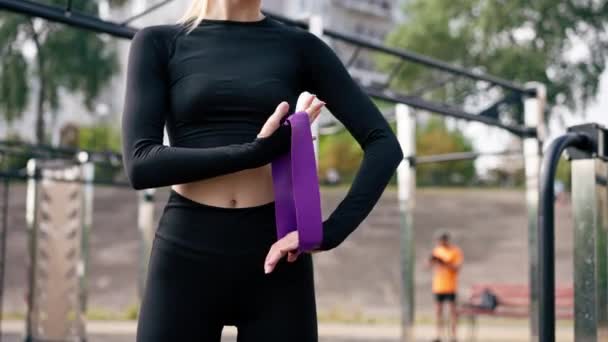 Primo piano di una ragazza che esegue esercizi con elastici rafforzare i muscoli del braccio durante l'allenamento in strada - Filmati, video