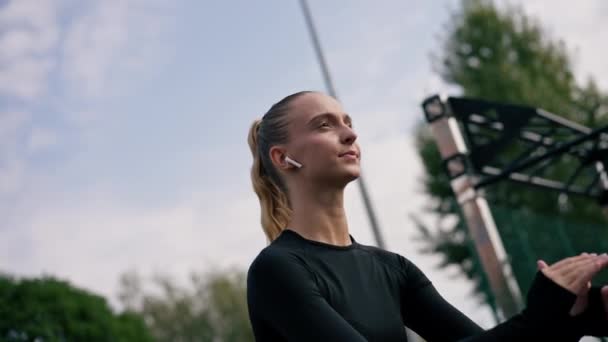 portrét zaměřený sportovní dívka ve sluchátkách dělat nohy cvičení dřepy s elastickou kapelou sportovní pole aktivní životní styl - Záběry, video