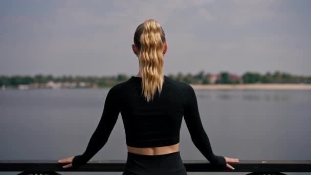 Een mooi meisje atleet tijdens het joggen gestopt op de brug in het park rust en geniet van het uitzicht achteraanzicht - Video