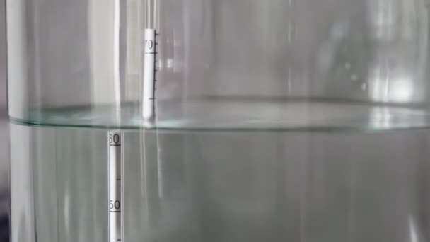 proceso de destilación de alcohol primer plano líquido destilado líquido transparente que fluye en un frasco de vidrio grande con alcoholómetro flotante en él. - Imágenes, Vídeo