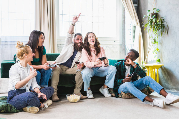 Multi-ethnic group of young boys and girls cheering after winning video games. Homely ambiance on the sofa during a fun day with friends. - Foto, immagini