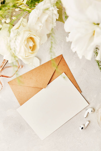 Beżowa papierowa koperta kreślarska, makieta na pozdrowienia, zaproszenie, pocztówka, tekst wśród białych kwiatów i słuchawek. Biofizyczne wnętrze, przytulny dom. Przestrzeń kopiowania - Zdjęcie, obraz