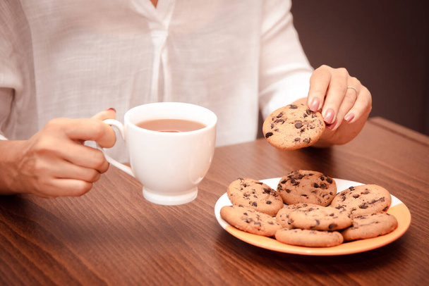 女性は仕事の休憩中にチョコレートチップとティーでクッキーを食べる - 写真・画像